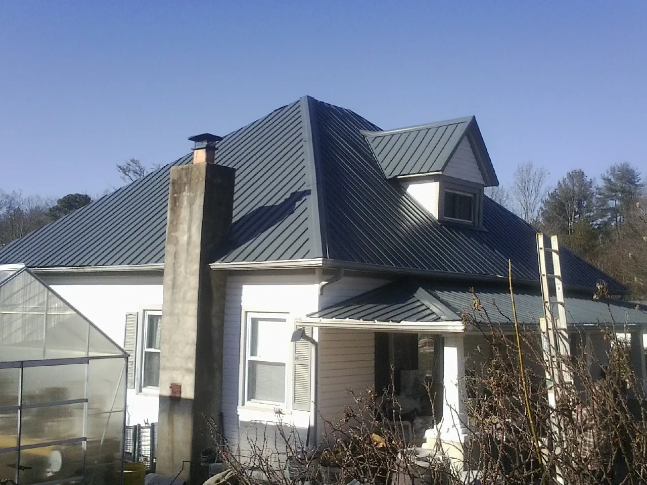 Dark blue standing seam metal roof on a white farmhouse with dormer — Slate & Tile Roof Repair by Roofing Brothers in Nedrow