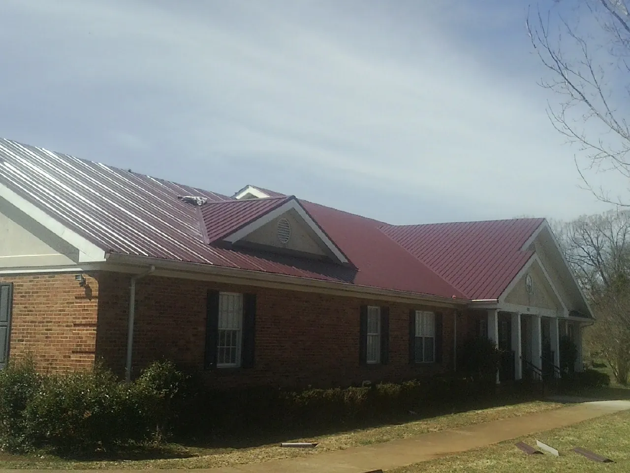 Red metal roof with gabled entries on a long brick building, from a Hail Damage Roof Repair job in Nedrow