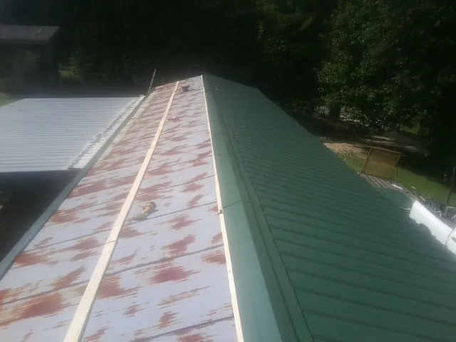 Old rusted panels beside newly installed green metal roofing — Wind Damage Roof Repair by Roofing Brothers in Nedrow