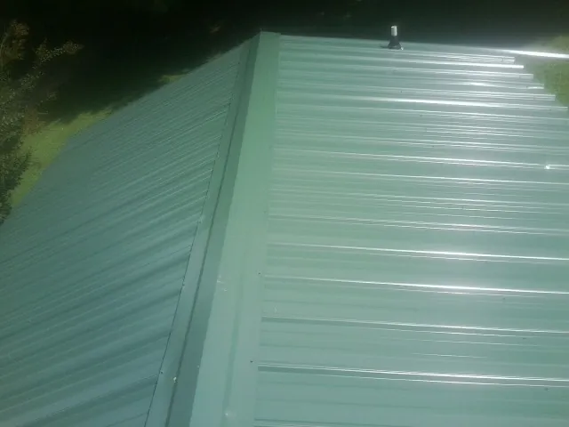 New green metal panels meeting at the ridge of a roof — Flat Roof Repair work by our crew in Nedrow