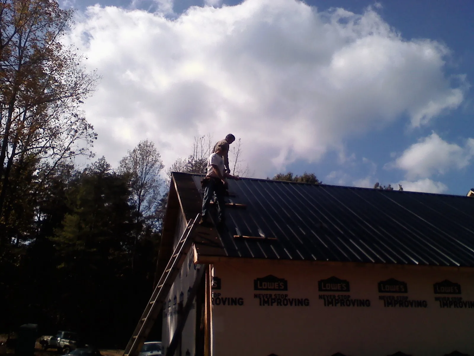 Roofer fastening dark metal panels high against a cloudy sky, from a Roof Inspection job in Nedrow