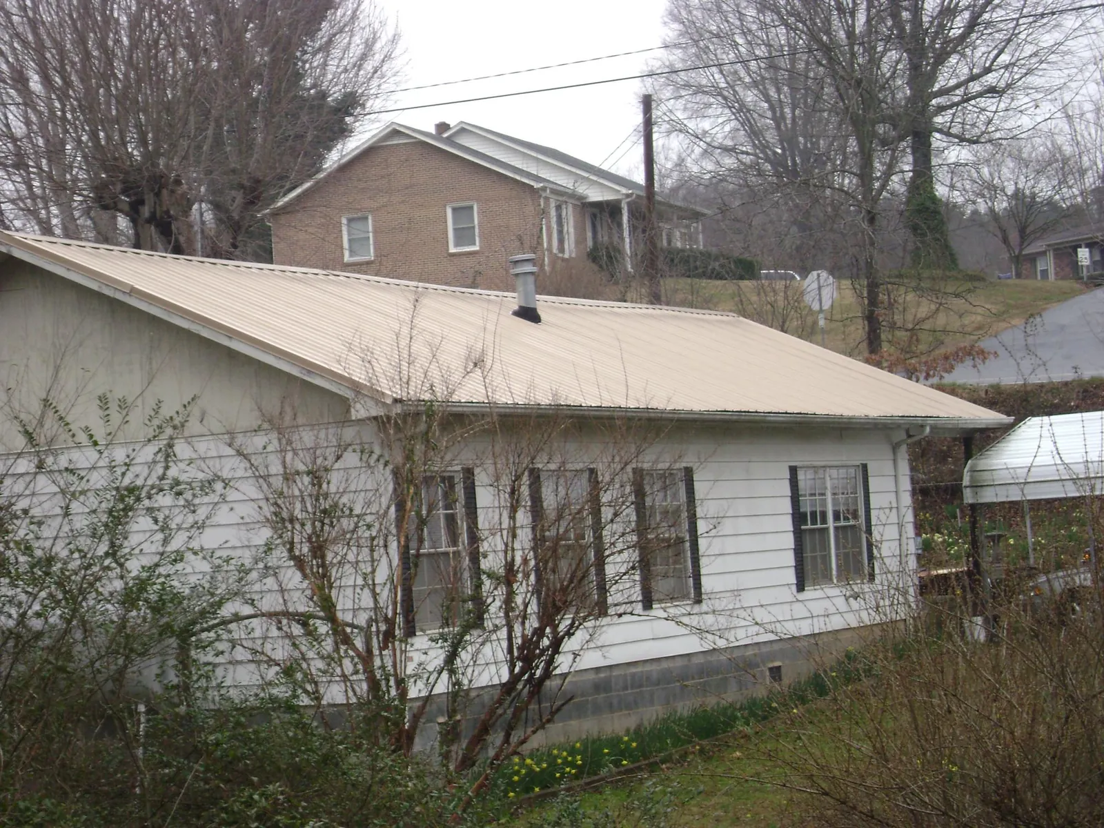 Tan metal roof on a white sided house set into a hillside — Commercial Roofing by Roofing Brothers in Nedrow